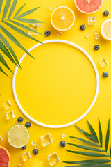Citrus mix concept. Top vertical view of mixed citrus fruits - orange, lemon, lime, and grapefruit with green palm leaves on a vibrant yellow background with empty circle for promotion