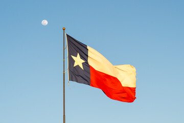 Flag of Texas waving in the wind with blue sky and moon in background. Texas is a state in the South Central region of the United States.