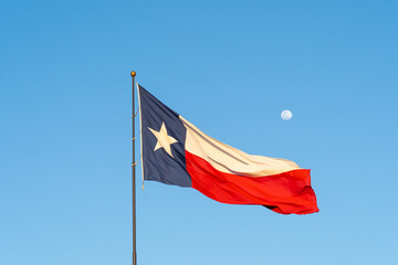 Naklejka na ściany i meble Flag of Texas waving in the wind with blue sky and moon in background. Texas is a state in the South Central region of the United States.