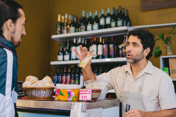 Middle-aged Latin salesman offering a cereal bar to a customer from the counter.
