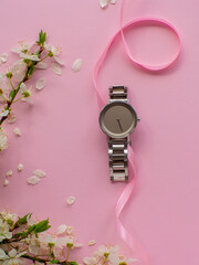 Womens hand watch on pink background with cherry flowers and copy space. Womens, Valentines and Mothers Day gift. Concept of beauty, elegance and femininity. Buying birthday gifts online.