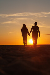 silhouette of a couple at sunset, woman and man walking along seashore in rays of sunset sunlight....