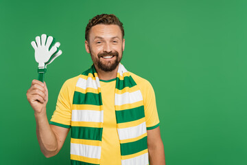 cheerful football fan in striped scarf holding plastic hand clapper isolated on green.