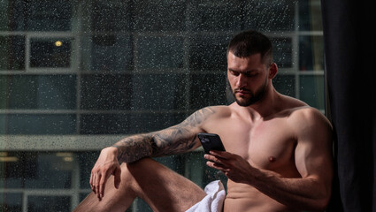 Man using phone standing near window. Seductive gay. Muscular body of man in hotel room. Sexy guy...