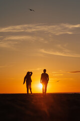 Fototapeta na wymiar silhouette of a couple at sunset, woman and man walking along seashore in rays of sunset sunlight. walk and hug. place for text, romantic relationships, freedom and carelessness