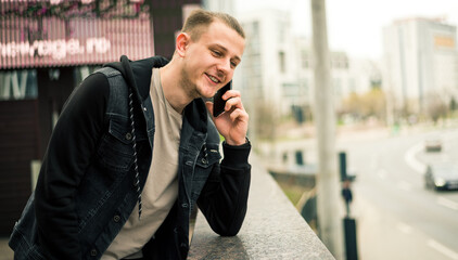 Cheerful young blonde hair student using mobile sitting at the city park.