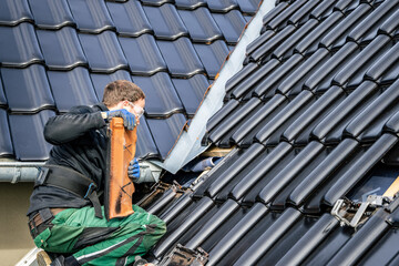 Craftsman removing tiles from a roof to install brackets for solar panels