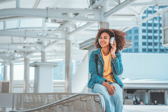 Young African American woman putting headphones and enjoying music on the urban city, Female listening to music on the town