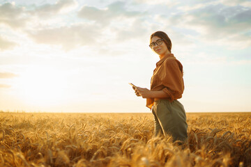 Young peasant woman in a golden wheat field with a clipboard checks the growth and quality of the crop. Growth dynamics. Agriculture or gardening concept.