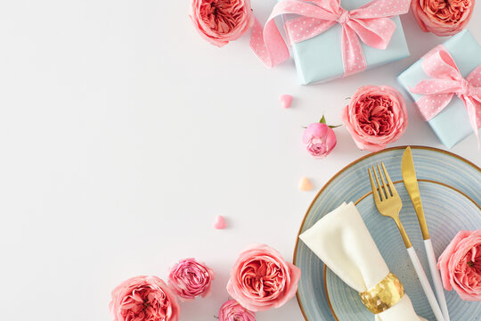 Festive setting concept for Mother's Day. Top view photo of plate cutlery knife fork napkin gift boxes natural flowers pink rose buds and small hearts on white background with empty space