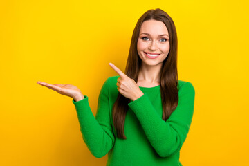 Portrait of nice cheerful person indicate finger arm hold empty space isolated on yellow color...