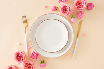 Top view photo of empty circle plate cutlery knife fork natural flowers pink rose buds and small hearts baubles on isolated light beige background. Women's Day concept