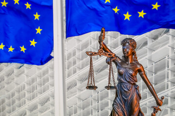 Themis and Europien Union flags on blurred buckground, shallow depth of field, focus on Themis statue. European Union law and jurisprudence