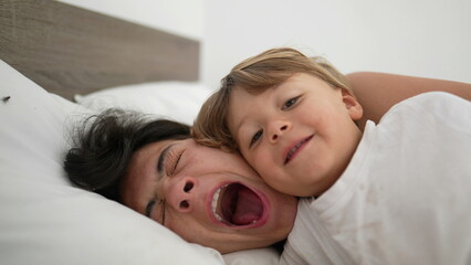 Mother yawning in bed waking up in the morning with child son. Tired motherhood lifestyle concept....