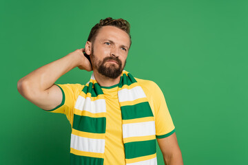 pensive soccer fan in striped scarf and yellow t-shirt looking away isolated on green.