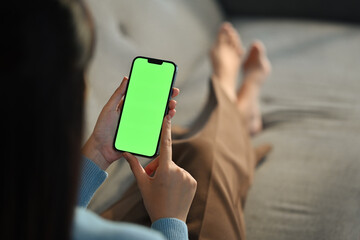 Young woman home use green screen mockup Smartphone, her sitting on sofa in living room