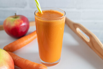 Carrot apple juice in a drinking glass with straw