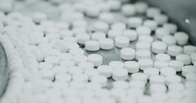 White pills moving on metal automatic line in workshop of pharmaceutical factory. Process of production of pills, drugs. Factory equipment and machine conveyor. Industrial pharmaceutical concept.