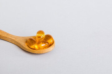 Vitamin omega capsules in a spoon on a colored background. Pills served as a healthy meal. Red soft gel vitamin supplement capsules on spoon