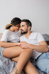 bearded man holding hands of pretty african american girlfriend while resting in bedroom at home.