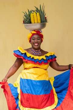 Cheerful fresh fruit street vendor aka Palenquera dancing in the Old Town of Cartagena, Colombia. Happy Afro-Colombian woman in traditional clothing, Colombian culture and lifestyle. 