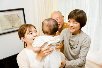 0歳の赤ちゃんを抱っこする母親と赤ちゃんをあやす祖父母