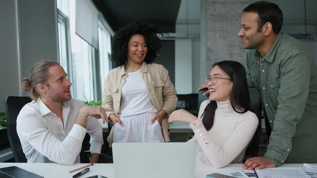 Laughing multinational colleagues discuss business development at meeting in conference room in office