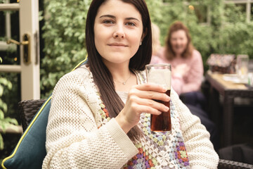Portrait of a mid-adult woman and new mother looking at camera having a non-alcoholic drink in a beer garden at the pub after a walk with her family. Spring time in Scotland. Leisure and relax.