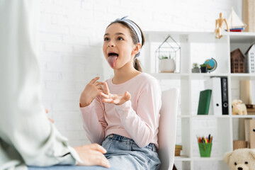 Preteen pupil sticking out tongue near blurred speech therapist in consulting room. © LIGHTFIELD STUDIOS
