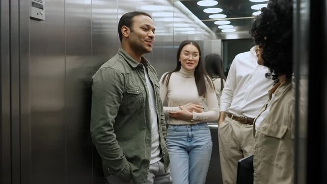 Cheerful multinational colleagues discussing work project and riding in elevator in office