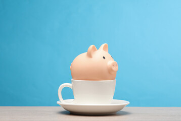 Fototapeta na wymiar Ceramic cup with piggy bank on the table, blue background
