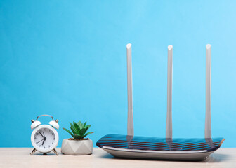 Three antenna wi-fi router with alarm clock, plant on the table, blue background