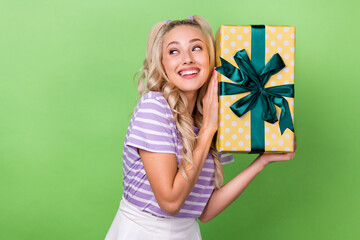 Photo of cute adorable girl with curly hairdo wear striped t-shirt holding present look empty space isolated on green color background