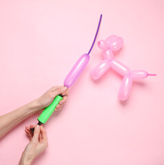 Hands inflate a long balloon with a pump to create different shapes and dog balloon on pink...