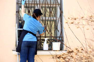 Window cleaning in city, woman washing the glass behind bars on old house facade