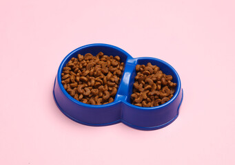 Double bowl of cat dry food on pink background. Top view