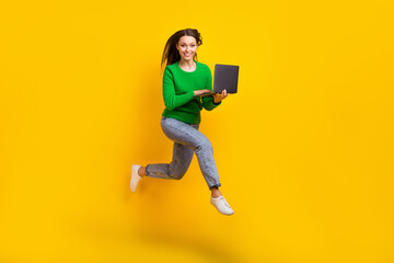 Full length photo of busy cheerful lady dressed green pullover jumping high texting modern device isolated yellow color background