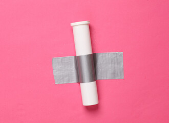 Pills tube fixed with adhesive tape on a pink background. Conceptual pop, contemporary art, minimalist still life
