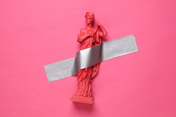 Antique statue of venus fixed with adhesive tape on a pink background. Conceptual pop, contemporary art, minimalist still life