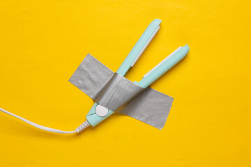 Hair iron fixed with adhesive tape on yellow background. Conceptual pop, contemporary art