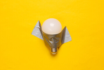 Light bulb fixed with adhesive tape on yellow background. Conceptual pop, contemporary art