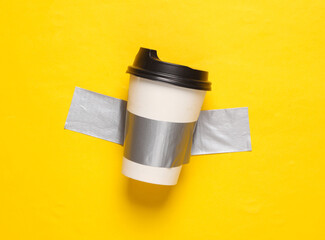 Coffee cup fixed with adhesive tape on yellow background. Conceptual pop, contemporary art