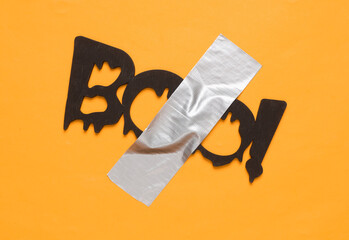 Word boo fixed with adhesive tape on orange background. Halloween concept. Conceptual pop, contemporary art, minimalist still life