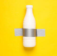 Milk bottle fixed with adhesive tape on yellow background. Conceptual pop, contemporary art