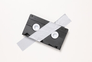 Video cassette fixed with adhesive tape on white background. Conceptual pop, contemporary art,...