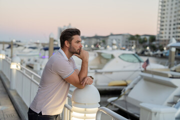 Rich business man dreaming and thinking near the yacht. Successful male model in big city living the urban lifestyle. Young male fashion model walking in street. Young hispanic man at the street.
