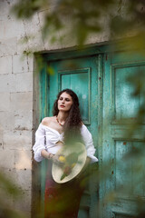 Beauty portrait of a sad curly girl dressed in a sensual clothes, holding in hands a straw hat with lemons, posing near old building and door.