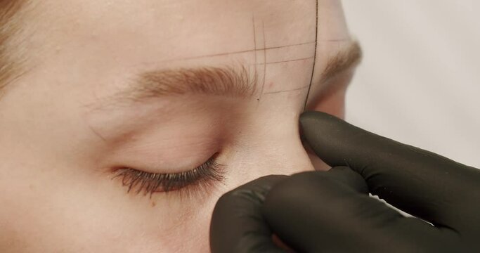 Cosmetologist marks the lines with a special thread to create the correct shape of the eyebrows during permanent makeup process. Cosmetologist making eyebrow permanent makeup.