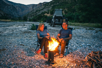 A woman and a man sit around a campfire in the evening and have fun.