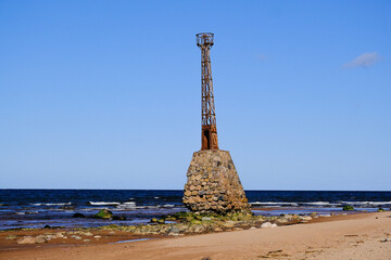 Fototapeta premium Ruins of the ancient Kurmrags lighthouse on the shore of the Gulf of Riga. Stone masonry in the lower part of the lighthouse, above which is the metal body of the lighthouse made in Sweden. Baltic Sea
